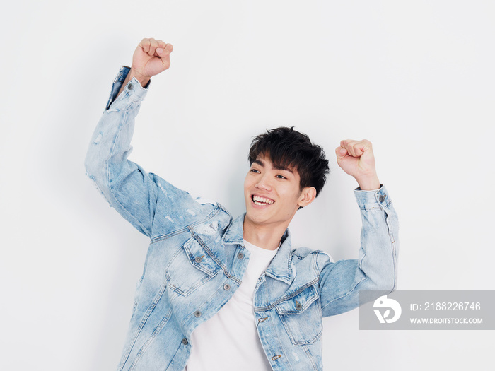 Portrait of handsome Chinese young man in blue jeans exciting with both arms up, crazy, casual man shouting with hands up above the head isolated on white background. Win or champion concept.