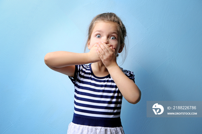 Cute little girl covering mouth with hands, on color background