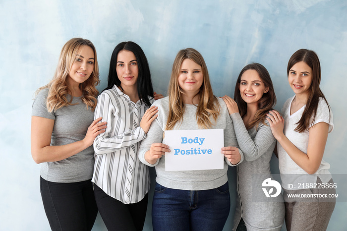 Beautiful young women holding paper sheet with text BODY POSITIVITY on color background