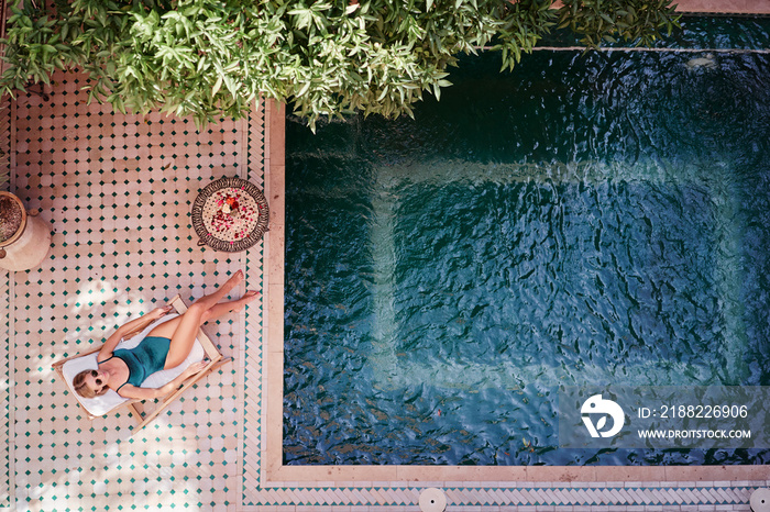 Enjoying suntan. Vacation concept. Top view of young woman near private swimming pool in beautiful moroccan backyard.