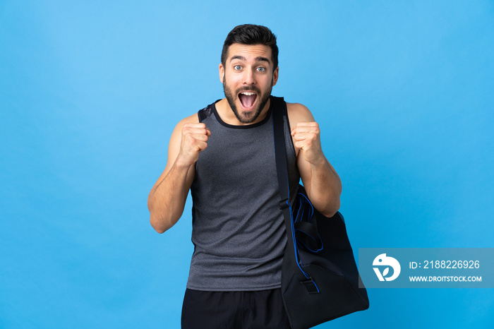 Young sport man with sport bag isolated on blue background celebrating a victory in winner position