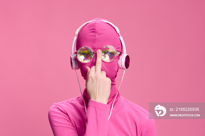 Conceptual creative art photo of a man in Total Pink on a pink background wearing a mask and glasses, who is adjusting his glasses with the middle finger of his hand