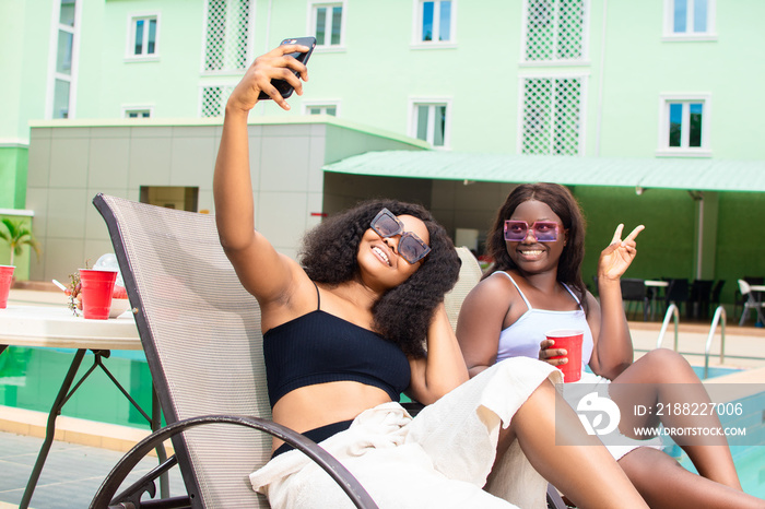 beautiful young african women on holiday relaxing by the pool taking selfies