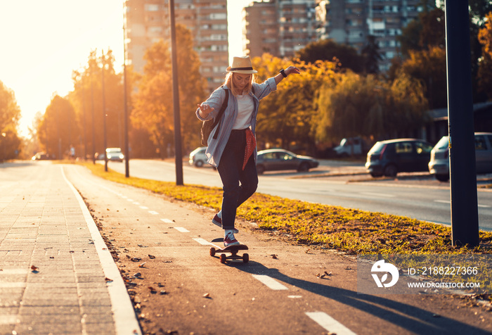 Smiling girl driving long board in the city during sunset.