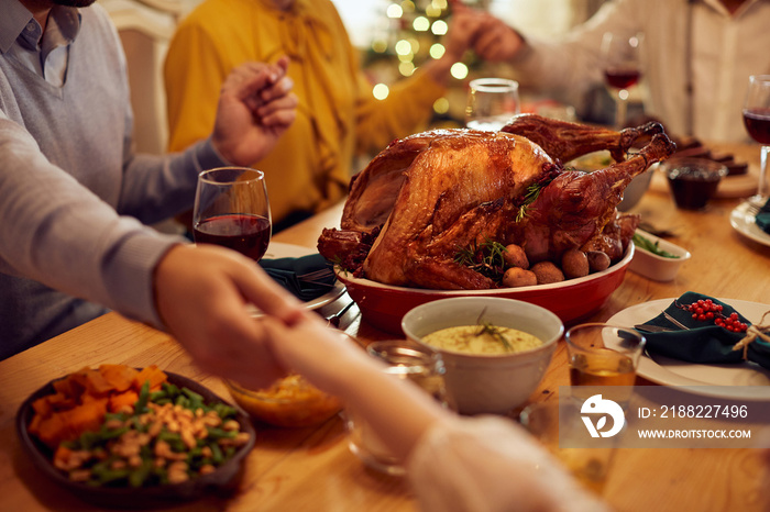 Close-up of family saying grace while holding hands during Thanksgiving meal at dining table.