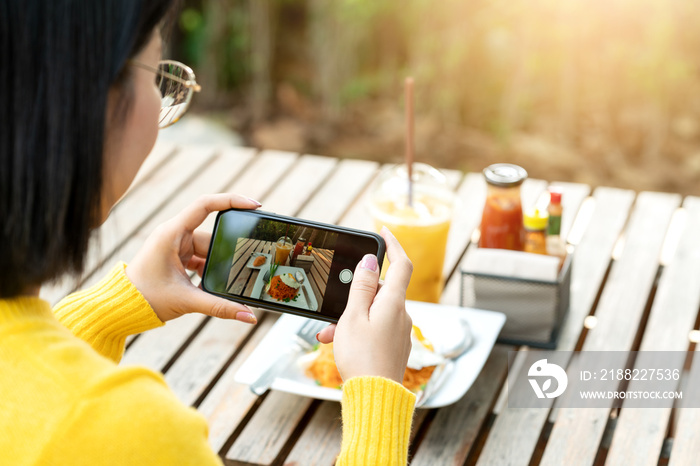 Young hipster asian blogger take photo of food, plate, healthy recipe, lunch meal, breakfast share to story in social media at restaurant or home. Screen showing on moblie phone with blogger concept.