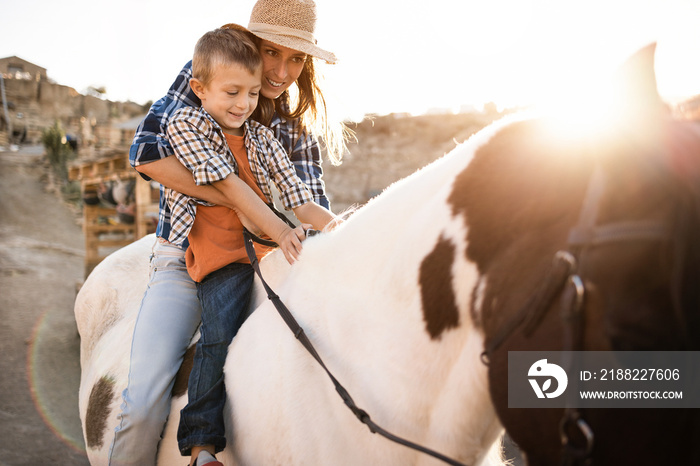 Happy mother and son riding a horse at sunset - Main focus on kid hands