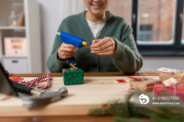 winter holidays and hobby concept - close up of woman with hot glue gun packing christmas gift or making advent calendar at home