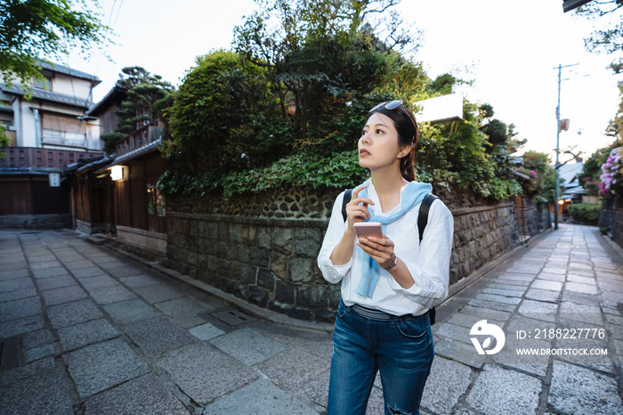 lost asian girl tourist is looking into distance feeling confused while using gps app on phone at the intersection of two lanes in historic district Kyoto japan