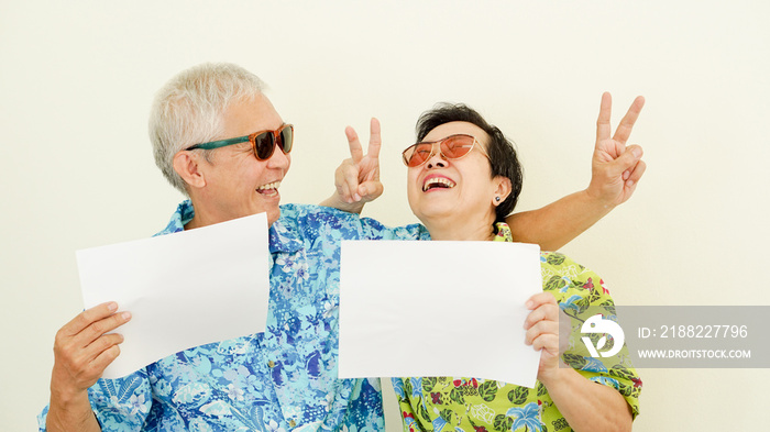 Senior Asian couple wearing holiday hawaii shirt holding white sign travel concept copy space