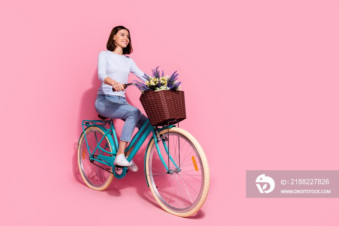 Photo of dreamy charming young woman wear white sweater driving bike looking empty space smiling isolated pink color background