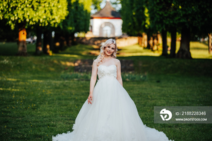 beautiful, blond bride standing and smiling in the park with a big, white dress