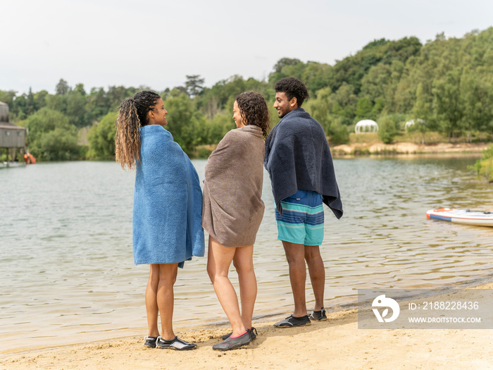 Friends wrapped in towels standing by lake