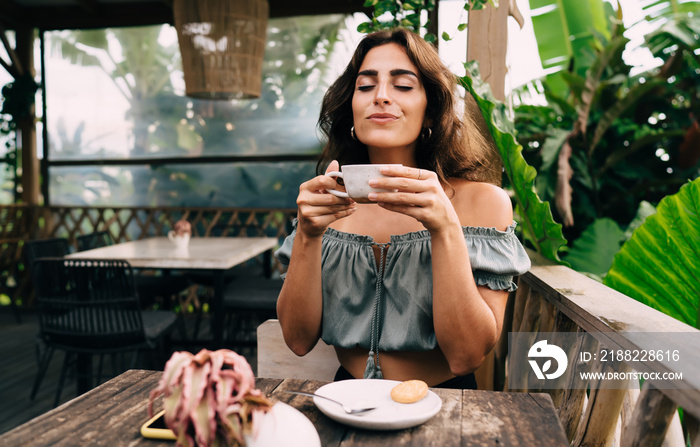 Satisfied ethnic lady with cup of coffee in tropical garden