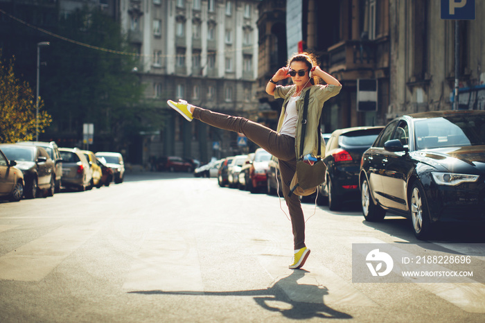 Cheerful woman listening to music via headphones and dancing on the street on a sunny day