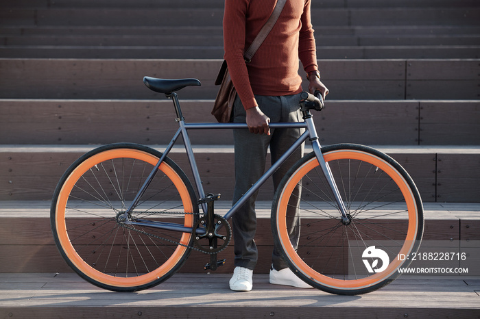 Low section of black guy with bicycle standing against staircase outdoors