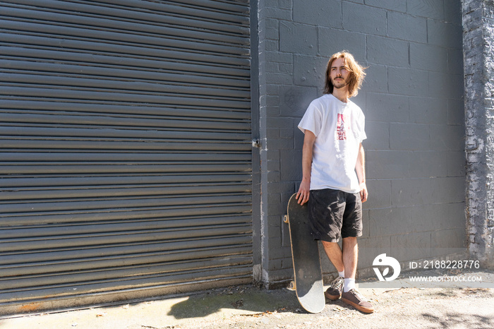 Young man standing outdoors holding skateboard