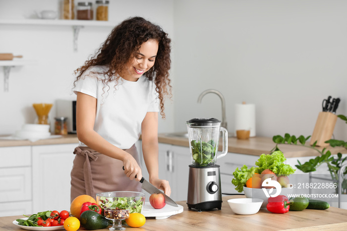 Young African-American woman cutting products for smoothie in kitchen