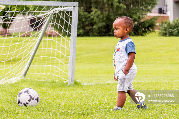 A little African toddler is playing soccer at summertime