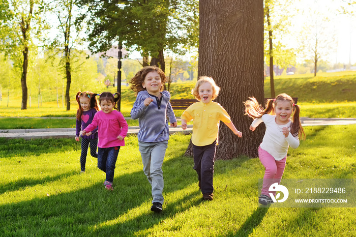 a group of small happy children run through the park in the background of grass and trees. Children’s outdoor games, vacations, weekend, Children’s Day, June 1