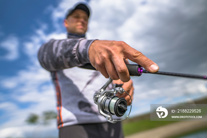 Fishing reel on spinning rod in hand blurred fisherman on skewed horizon