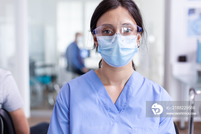 Worried nurse with face mask against coronavirus sitting on chairs in hospital waiting room. Doctor consulting senior man in examination room. Physician, epidemic, care, surgical, corridor.