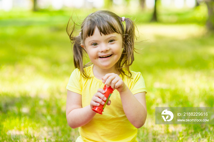 Portrait of a laughing girl with syndrome down blowing bubbles in a summer park