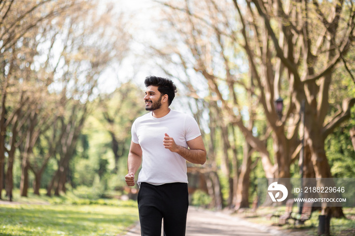 Strong muslim man in activewear running alone at green summer park. Handsome bearded guy spending leisure time for outdoors workout.