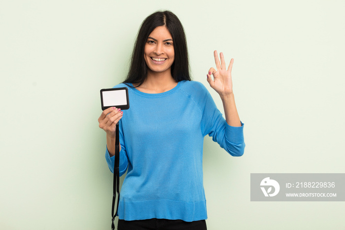 young pretty hispanic woman feeling happy, showing approval with okay gesture. accreditation pass id concept