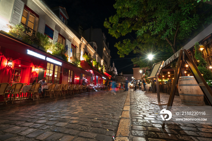 Typical night view of cozy street with tables of cafe and easels of street painters in quarter Montmartre in Paris, France