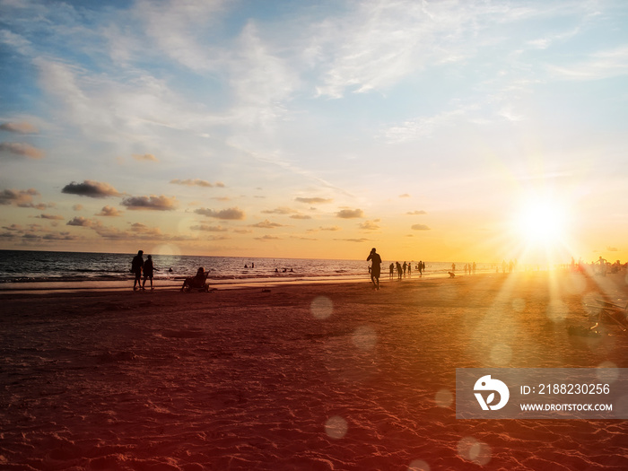 group of silhouetted people on public beach over orange colored sunset sky in Siesta key, Sarasota, Florida