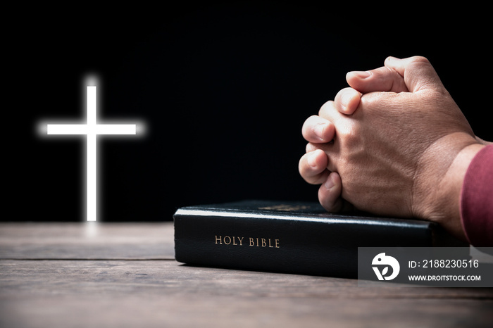 Hands folded in prayer on Holy Bible with cross in church concept for faith, spirituality and religion, Man praying on holy bible withcrucifix in morning. Man hand with Bible and rood praying to god.