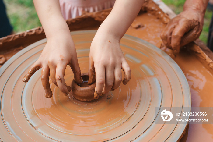 Potters and child hands. Pottery workshop outside. Master teaching kid to creating on the pottery wheel.