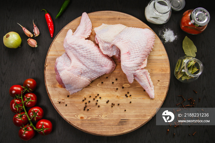 Poultry meat. Turkey wings lie on a wooden board. Chicken wing with peppers and tomatoes on a black background.