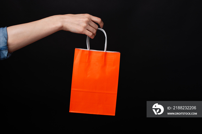 Woman hand holding orange shopping bag over black background