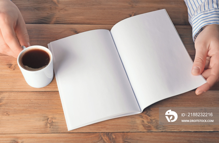 Female hands holding blank brochure  and cup of coffee on wooden background