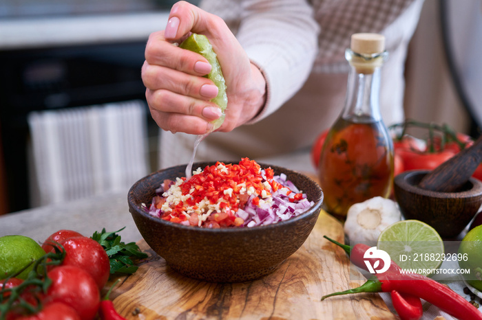 making salsa dip sauce - woman squeezing fresh lime juice to chopped ingredients in wooden bowl