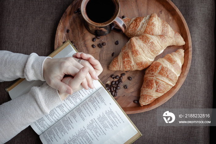 hands in prayer with bible, coffee and croissants