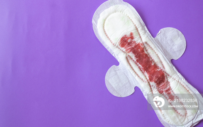 feminine sanitary napkin with blood simulation, on a purple plain background.