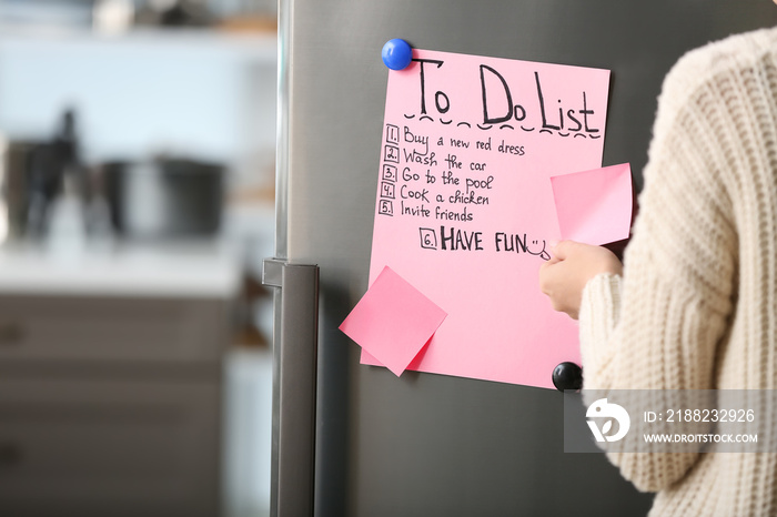 Woman checking to-do list on fridge in kitchen