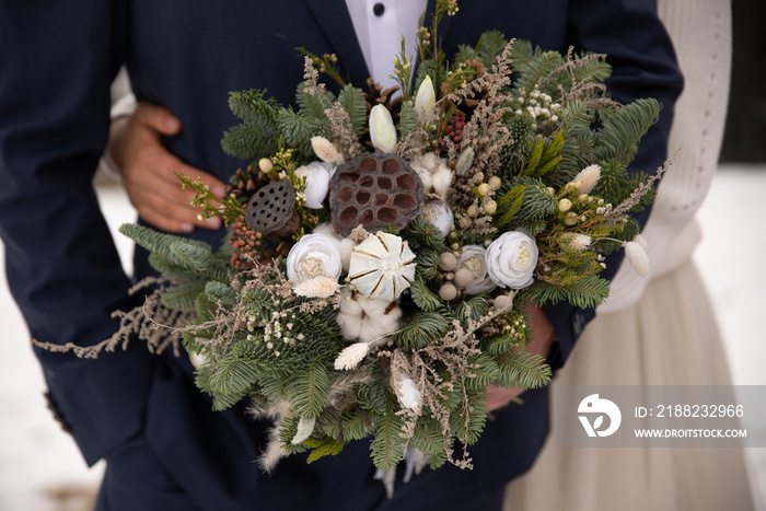 Couple of groom and bride in white wedding dress  flowers bouquet in hands and embracing outdoors. Winter wedding and season floral concept.