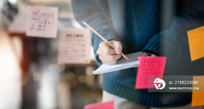 businesswoman writing note and using post it notes in glass wall, strategy business plan to development grow to success.