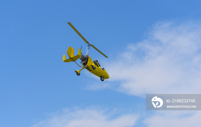 Yellow gyrocopter in air on blue sky and clouds