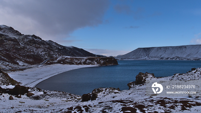 Beautiful view of the northern part of lake Kleifarvatn in Krýsuvík, Reykjanes peninsula, Iceland with rocky beach, country road and snow-covered mountains in winter season.