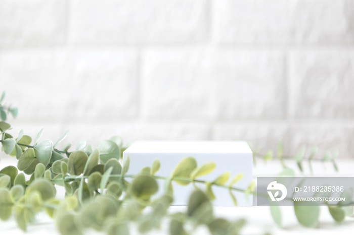 Empty podium or pedestal with chamomile green leaves on a white brick background. Blank shelf product standing for display