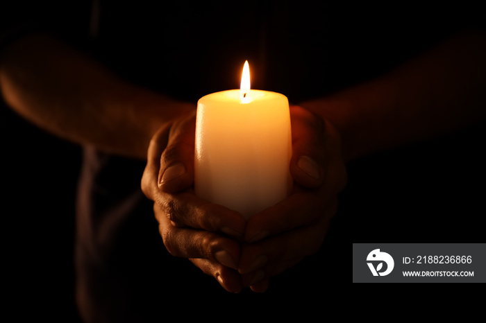 Young man holding burning candle in darkness