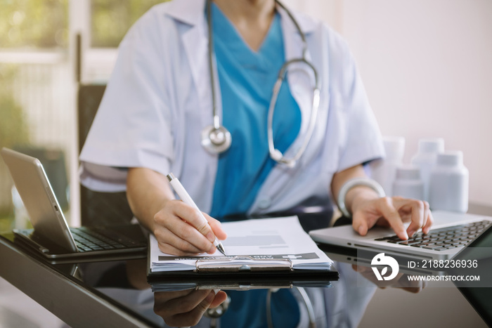 Doctor working on laptop computer and tablet and medical stethoscope on clipboard on desk, electronics medical record system EMRs concept.