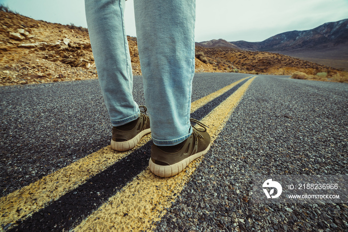 Man ready to take a new way and make a step to new life concept. Feet on empty and free aspalt road in desert.