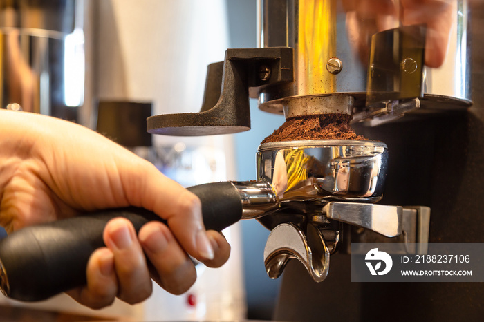 Close up woman hand holding portafilter, girl barista is grinding the roasted coffee beans into powder using coffee grinder at cafe shop