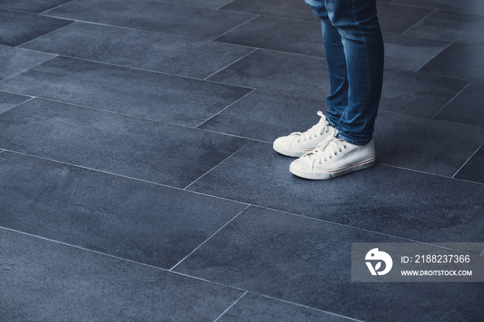 Close up woman standing on dark grey tile floor wear white sneaker canvas shoe.